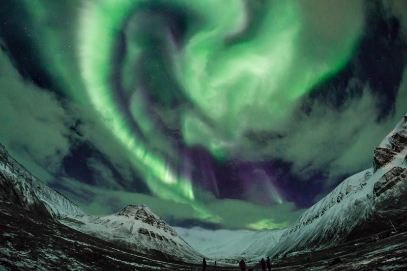 A couple of people standing in front of a green and purple Northern Lights 